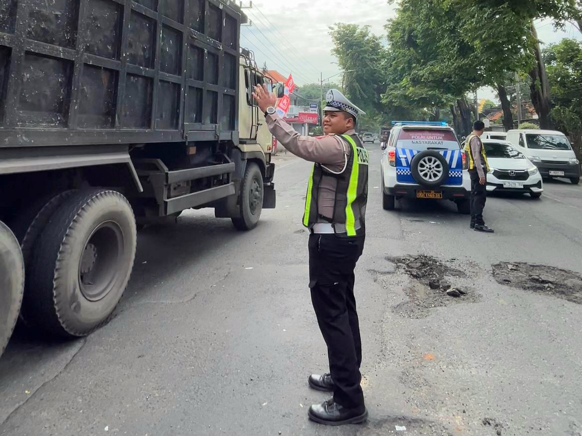 BANYAK DIKELUHKAN: Personel Satlantas Polres Pasuruan mengatur lalu lintas saat jalan berlubang di Bangil dibenahi sementara. Jalan berlubang di titik ini bakal dibenahi.