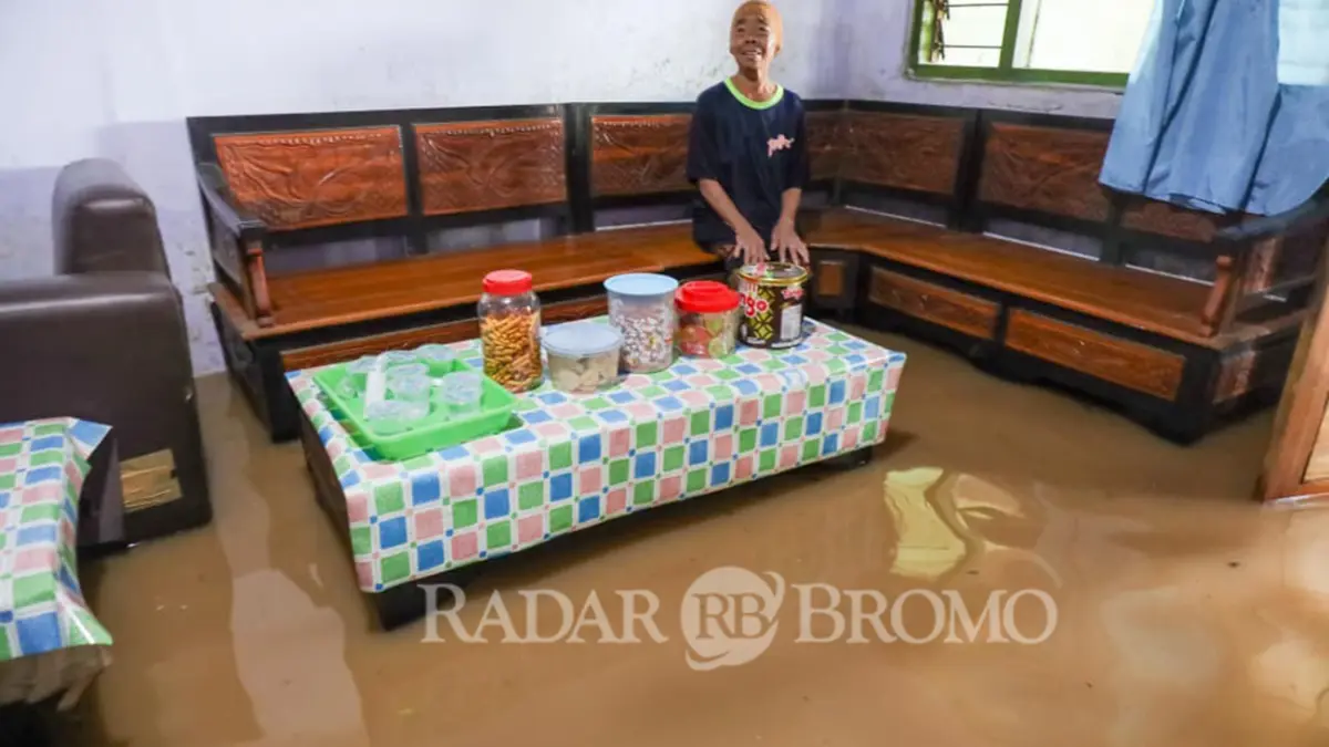 KEDATANGAN "TAMU" TAK DIUNDANG: Salah satu warga bersantai di ruang tamu rumahnya dengan kue lebaran yang masih tersaji dalam kondisi banjir. (Mokhamad Zubaidillah/ Radar Bromo)