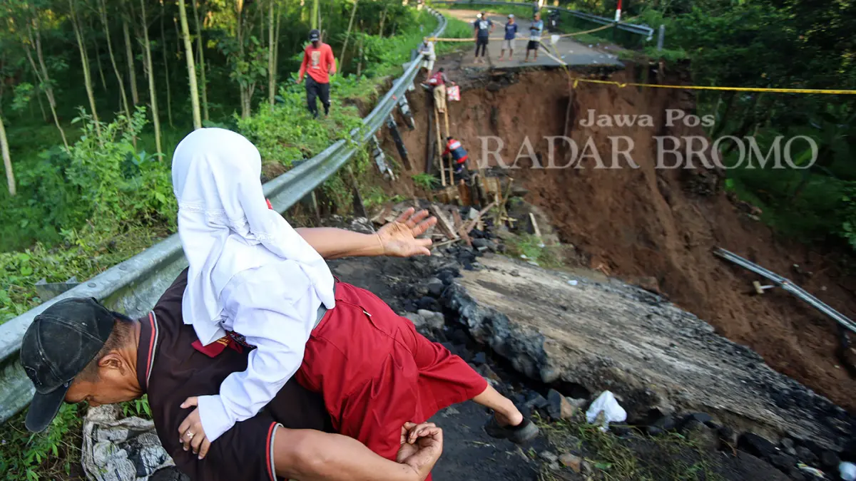 SEMANGAT: Siswi kelas 1 SDN 2 Lumbang Nadira dibantu warga sekitar menuruni tebing Jembatan Duren, Desa Negororejo, Kecamatan Lumbang, Kabupaten Probolinggo, yang sudah ambruk untuk menuju sekolah Senin (30/3) pagi. (Mokhamad Zubaidillah/ Radar Bromo)
