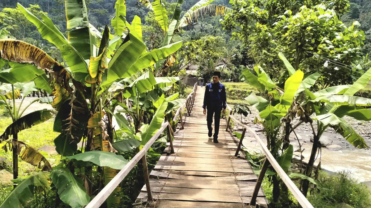 MENGKHAWATIRKAN: Bendahara Desa Andungbiru Agus Santoso menyeberangi jembatan RT 3/RW 1, Dusun Krajan. Jembatan ini segera direhab agar lebih aman. (Achmad Arianto/Jawa Pos Radar Bromo)