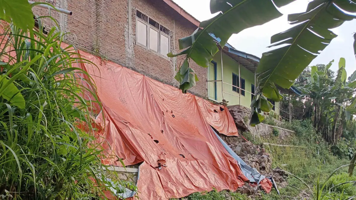 DITUTUP TERPAL: Tembok penahan tanah di yayasan Ainur Rohmah di Desa Tambak Ukir yang ambrol. Sejauh ini belum ada penanganan. (Foto: Istimewa)