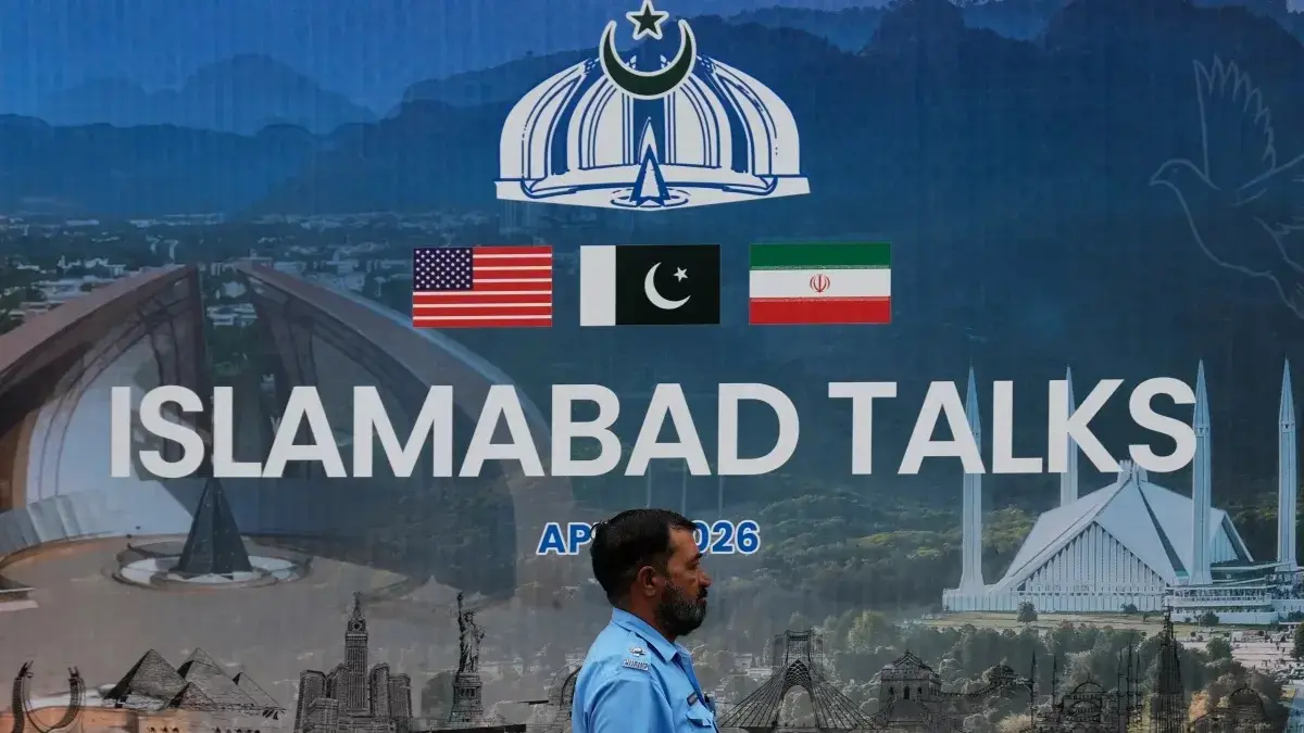 Seorang petugas polisi berjalan melewati papan iklan mengenai negosiasi Amerika Serikat dan Iran, di luar pusat fasilitasi media di Islamabad, Pakistan. (Anjum Naveed/AP)
