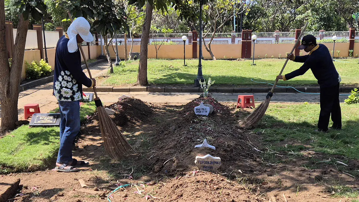 BERSIHKAN: Petugas kebersihan makan di TPU Purut III saat tengah bersih-bersih makam. (Fahrizal Firmani/Radar Bromo)