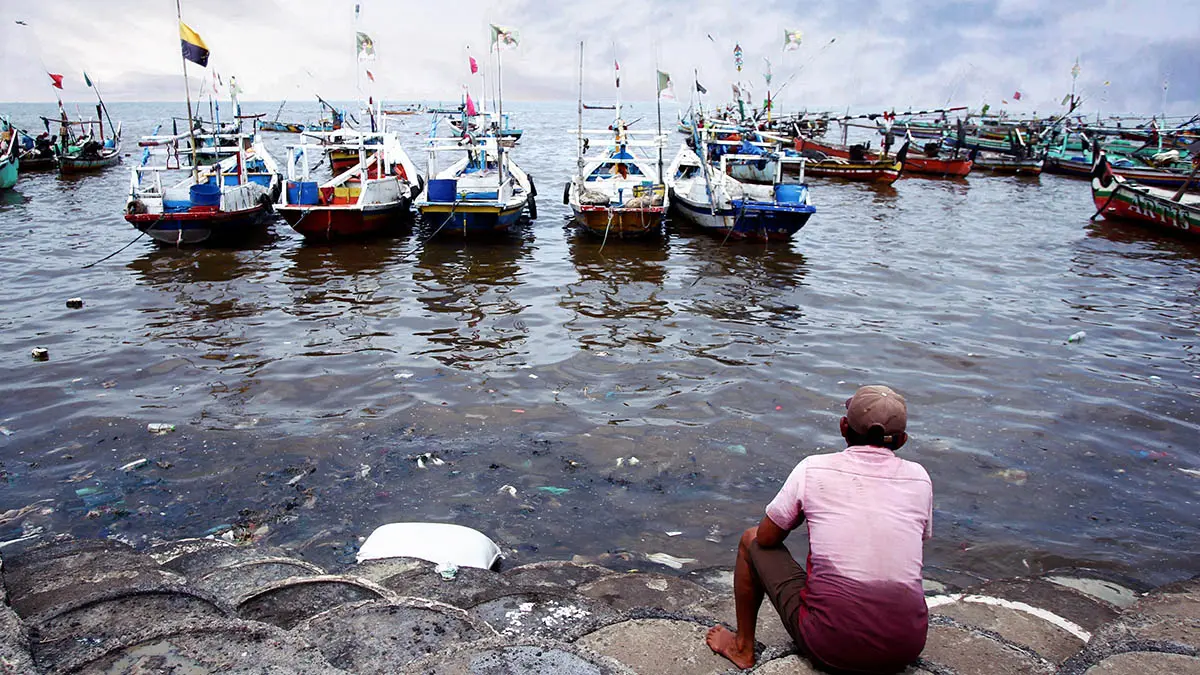 TAK MENENTU: Seorang nelayan yang duduk di bebatuan tepi laut Lekok. BMKG mengingatkan, untuk tetap mewaspadai risiko bencana imbas cuaca yang berubah-ubah. (Mokhamad Zubaidillah/Radar Bromo)