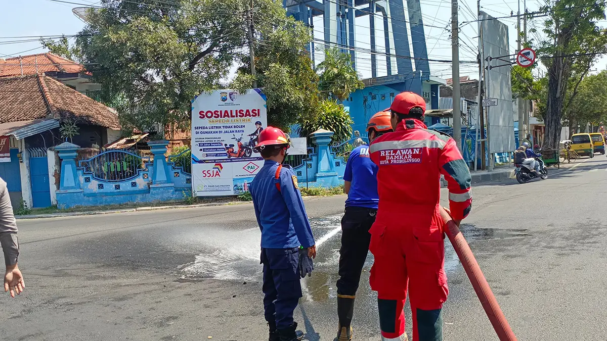 SAPU: Tim Damkar Satpol PP Kota Probolinggo membersihkan tumpahan batu bara di Simpang Empat Randupanger, Kota Probolinggo, Jumat (17/7). (DAMKAR SATPOL PP KOTA PROBOLINGGO for JAWA POS RADAR BROMO)