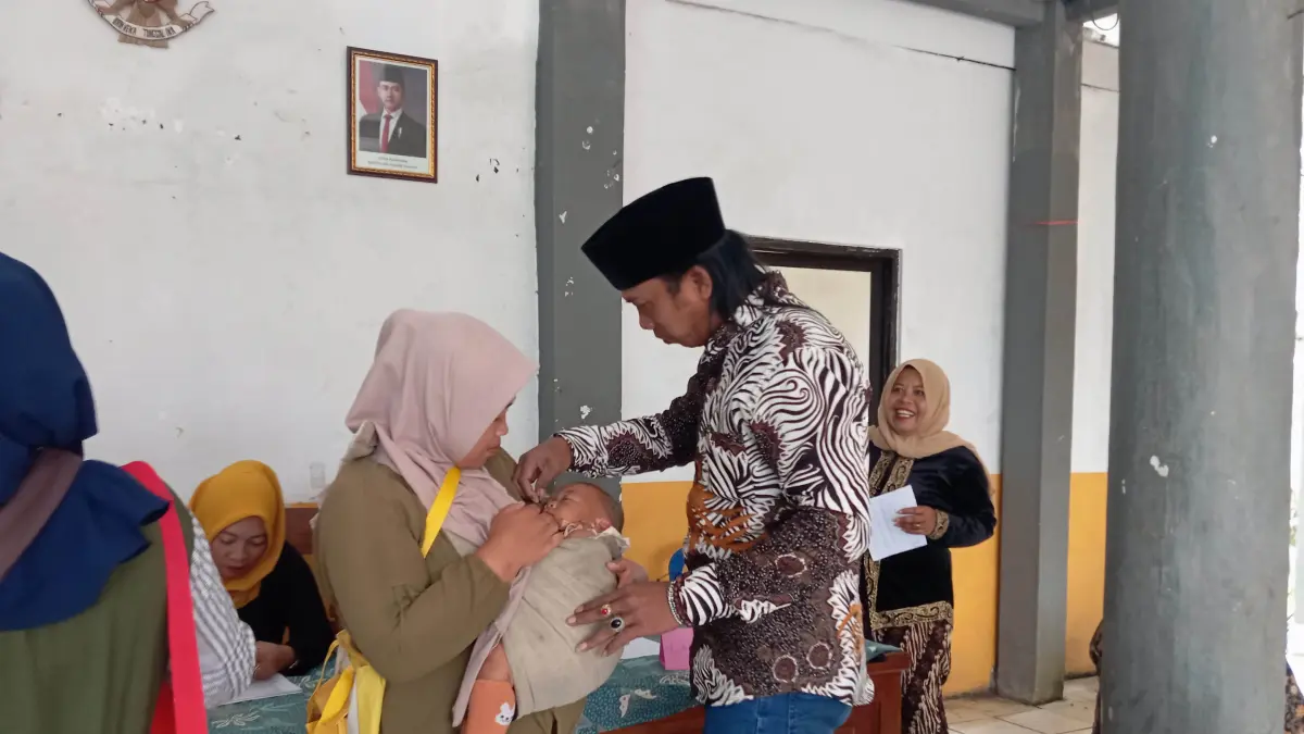 VITAMIN: Kepala Desa Sapih Ngatiman memberikan vitamin kepada seorang balita dalam kegiatan Posyandu di Balai Desa Sapih.