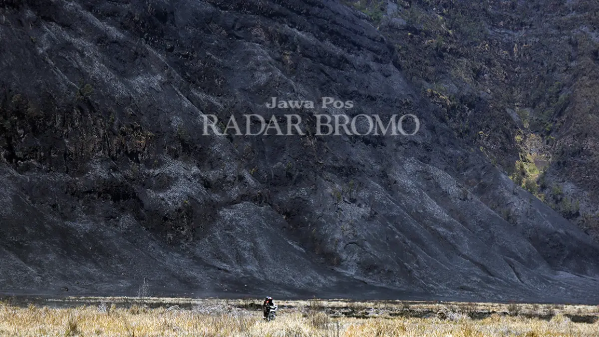 HANGUS: Pengendara motor melintasi kawasan sabana Bromo dengan latar belakang bukit di kawasan Gunung Bromo yang hangus usai terbakar, Senin (10/8). (Mokhamad Zubaidillah/ Radar Bromo)