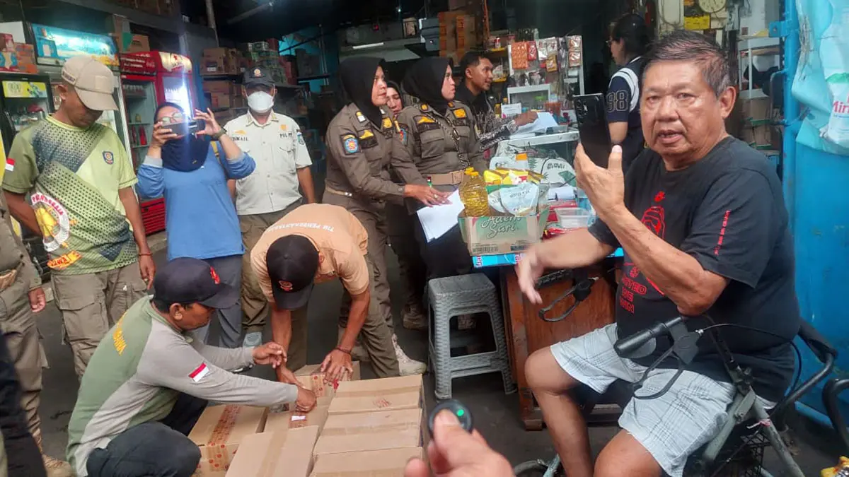 Petugas Satpol PP saat membuka sejumlah karton berisi miras. Sementara sang pemilik toko Tjan Jun mengabadikan momen tersebut. (Arif Mashudi/ Radar Bromo) 