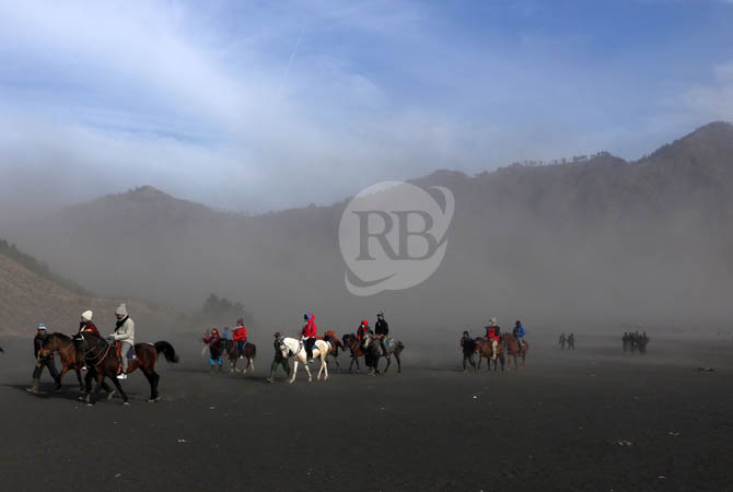 Para wisatawan melintas di lautan pasir Gunung Bromo yang diterjang badai pasir, Minggu (20/10) siang. Para pengunjung dihimbau mengenakan masker dan kaca mata lantaran sejak beberapa hari terakhir kawasan ini kerap diterjang angin kencang.