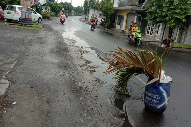 MEMBAHAYAKAN: Warga memasang pot di jalan Pandaan-Bangil di Desa Baujeng yang alami kerusakan. (Istimewa)