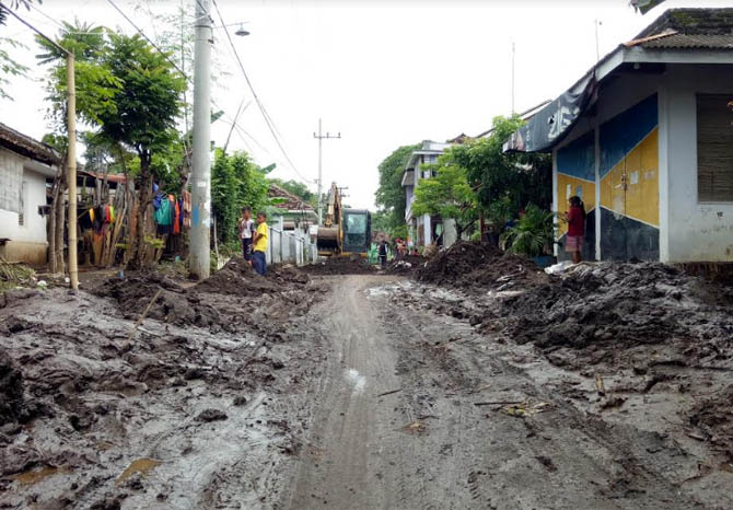 DIBERSIHKAN: Petugas menggunakan alat berat membersihkan lumpur yang menutupi akses utama jalan Desa Sekarputih, Kecamatan Gondang Wetan, Kabupaten Pasuruan, Kamis (7/1). (Foto Mukhamad Rosyidi/Jawa Pos Radar Bromo)