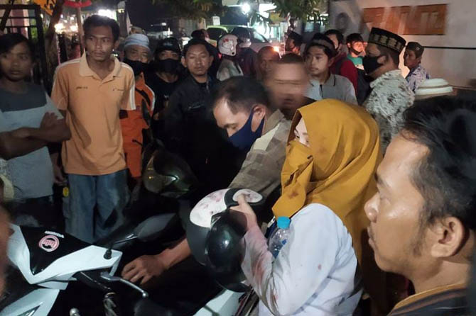 JADI PERHATIAN: Sejumlah warga mengamankan NR (berkerudung), setelah dihantam menggunakan gelas oleh suaminya, Rabu (6/1) sore. (Kartika For Jawa Pos Radar Bromo)