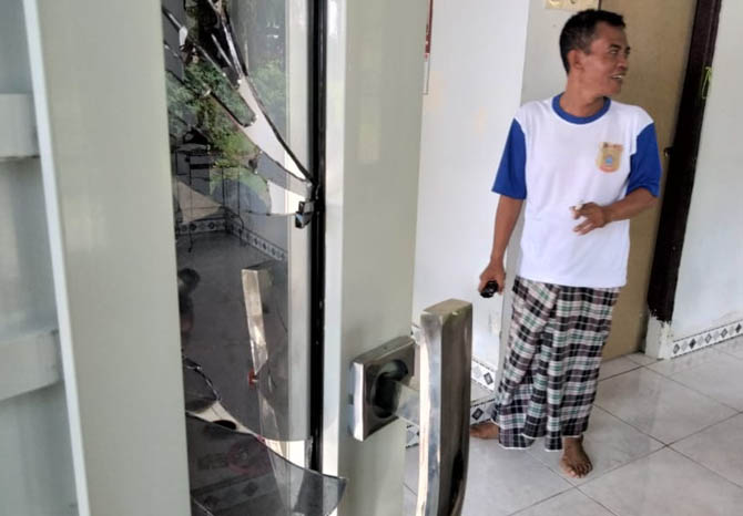 RUSAK: Bukhori menunjukkan kaca pintu depan rumahnya yang pecah karena terkena bondet. Selain itu, pintu samping rumahnya jebol. (foto M Busthomi/Jawa Pos Radar Bromo)