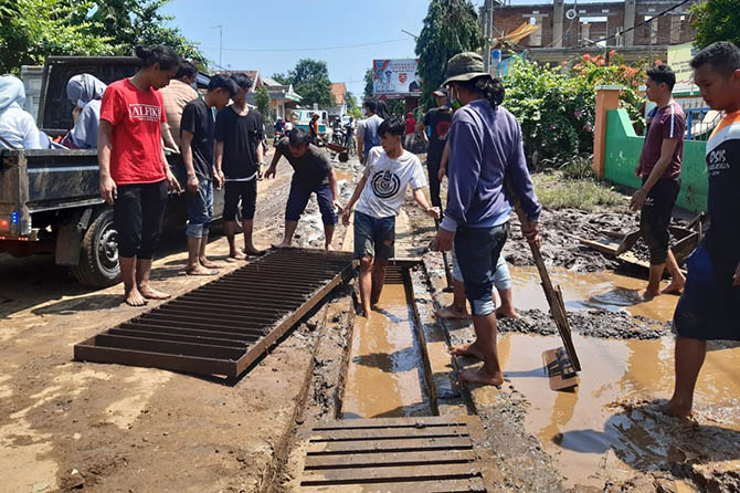 BERSIH-BERSIH: Warga dan relawan tengah bersih-bersih selokan saluran air di jalan kabupaten Desa Dringu. (Arif Mashudi/Radar Bromo)