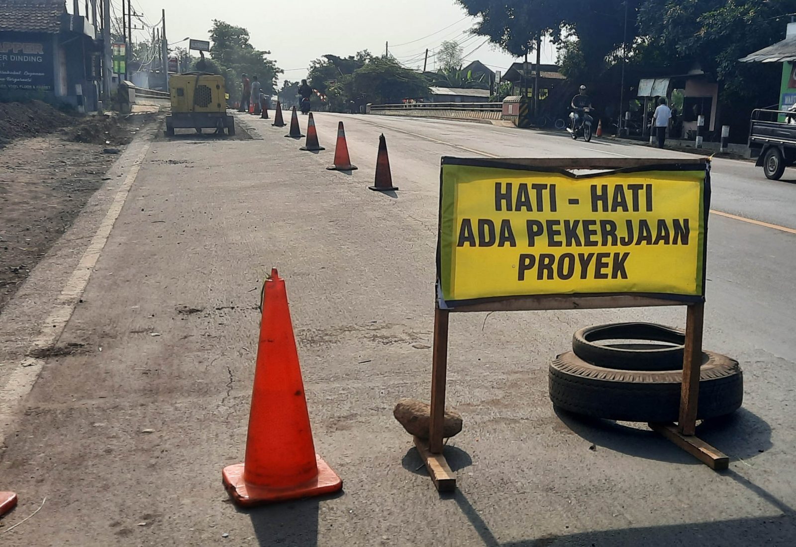PERBAIKI LUBANG: Tanda yang dipasang di sekitar jembatan Rejoso. Nampak Kamis pekerja menambal lubang di jalan. (Foto: Fahrizal Firmani/Jawa Pos Radar Bromo)