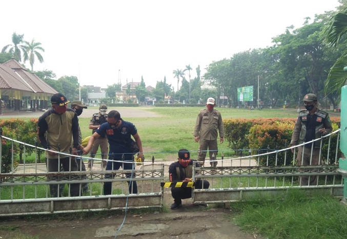 HANYA SEMENTARA: Sejumlah anggota Satpol PP Kabupaten Pasuruan memasang garis Satpol PP di Alun-alun Bangil, Minggu (4/7). Ruang publik ini akan ditutup selama PPKM Darurat. (Satpol PP Kabupaten Pasuruan for Jawa Pos Radar Bromo)