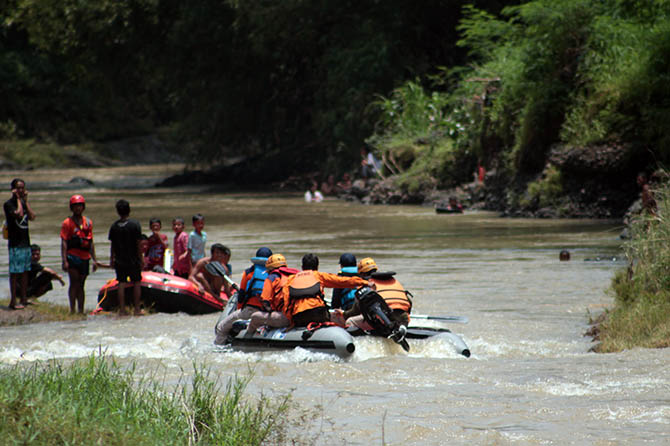 BELUM MEMBUAHKAN HASIL: Tim penyelamat menggunakan perahu karet untuk menyisir sungai saat mencari keberadaan korban. Tampak warga ikut memantau pencarian dari tepi sungai. (Agus Faiz Musleh/Radar Bromo)