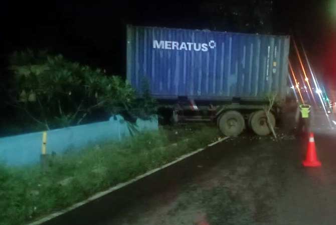 Kondisi truk kontainer yang menabrak pagar makam di tepi jalan. Sebagian besar kabin truk masuk ke makam.