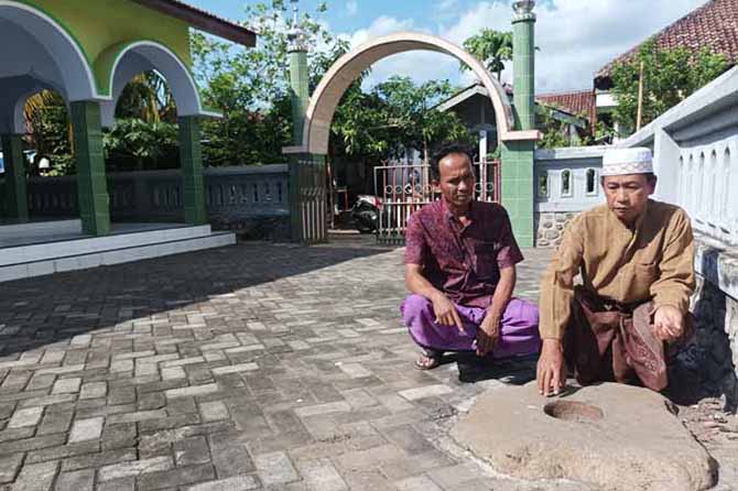 BATU LESUNG: Kasun Krajan Muhammad Saihu (kiri) bersama Badri, takmir Masjid Ar-Rohmah di depan batu lesung. (Foto: Agus Faiz Musleh/Jawa Pos Radar Bromo)
