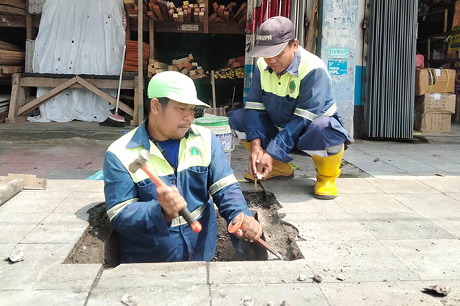 BUAT BARU: Petugas Dinas PUPR Kota Pasuruan membuat penutup drainase dari cor setelah penutup dari pelat besi di Jalan Hasanuddin hilang. (Muhamad Busthomi/Radar Bromo)