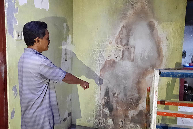LOKASI KEJADIAN: Sutari menunjukkan lokasi televisinya yang meledak di ruang tengah rumahnya. Terlihat dinding rumahnya terdampak percikan api. (Fahrizal Firmani/Radar Bromo)