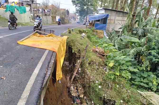 BERBAHAYA: Warga memasang penanda dan terpal di plengsengan tepi jalan yang alami longsor pada Desember tahun lalu. (Rizal f. Syatori/ Radar Bromo)