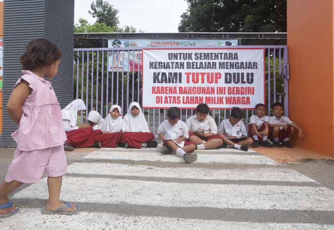 TAK BISA MASUK: Sejumlah siswa SDN Kalirejo 2 di depan gerbang sekolah. Nampak pagar yang ditutup dan terpaang bahwa sekolah ditutup ahli waris pemilik lahan. (Foto: Zainal Arifin/Jawa Pos Radar Bromo)