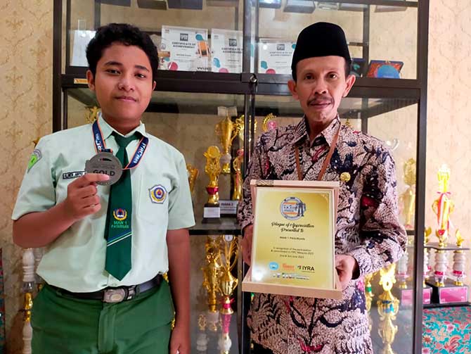 JUARA PERTAMA: Almer Abiyu Ahmad bersama Kepala MAN 1 Pasuruan Nasrudin menunjukkan penghargaan yang diraih dalam ajang International Youth Robotic Competition 2023 di Malaysia. (Iwan Andrik/Radar Bromo)