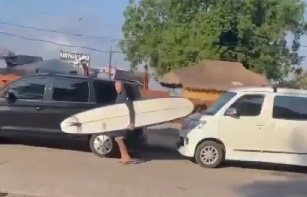 Tangkapan layar bule tenteng papan surfing gores body mobil yang berjejer diduga di Pantai Legian, Badung Bali.