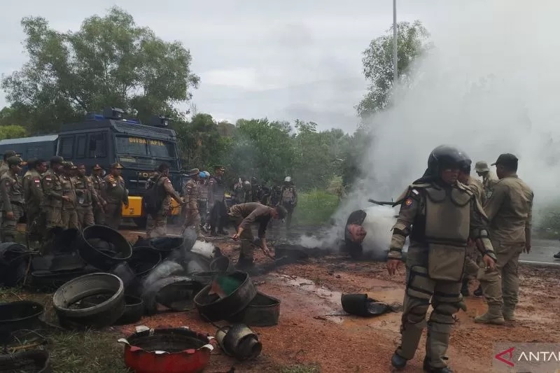 PETUGAS: Petugas gabungan membersihkan tumpukan ban yang dibakar warga di lokasi konflik di Pulau Rempang, Batam.