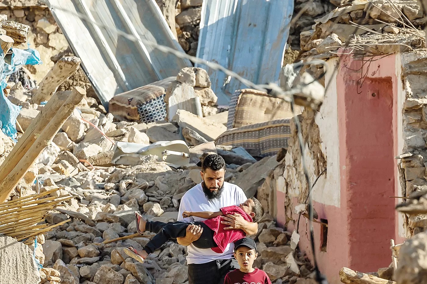 DUKA UNTUK MAROKO: Seorang pria menggendong bocah laki-laki melewati rumah-rumah yang hancur setelah gempa di Desa Pegunungan Tafeghaghte, barat daya Marrakesh.