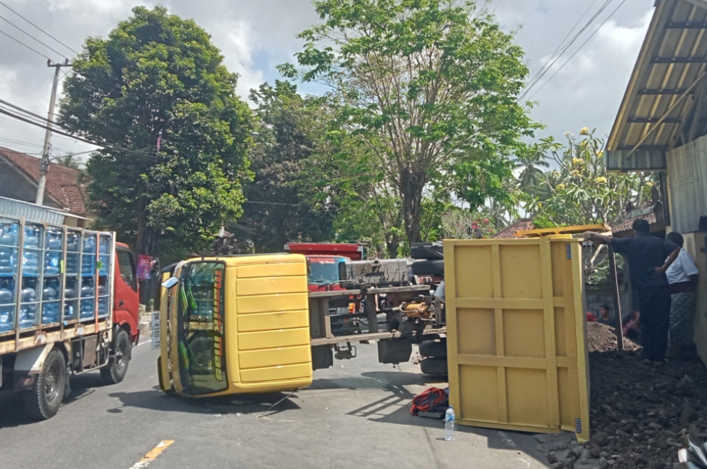TERGULING: Truk muatan tanah terguling di Jalan Ahmad Yani, Amlapura, Selasa (19/9). Kejadian ini membuat arus lalulintas terhambat.