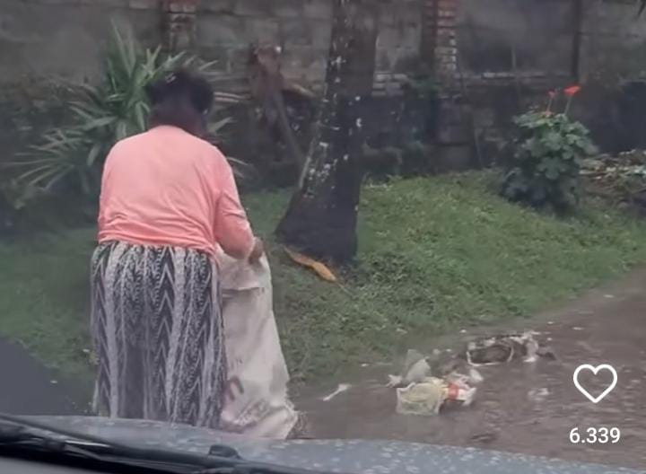 Seorang nenek membuang sampah plastik di aliran banjir