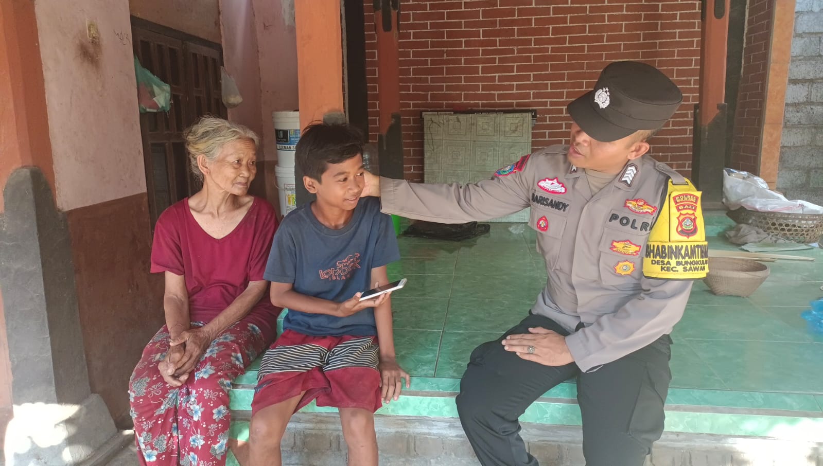 Bhabinkamtibmas Desa Bungkulan, Bripka I Putu Harisandy Mahayuda saat memberikan ponsel.