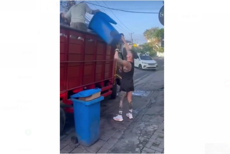 Seorang bule membantu seorang warga mengangkat sampah ke truk pengangkut sampah