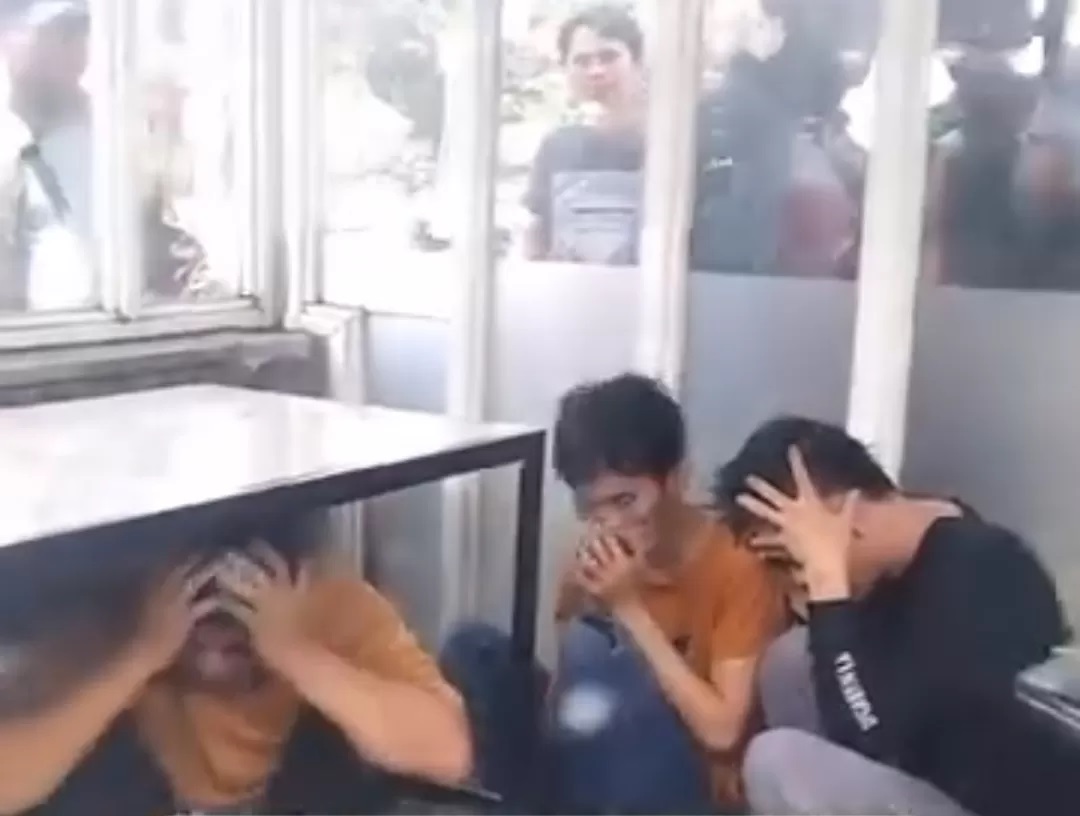 Pengemudi dan penumpang Sigra BE 1715 VE yang sembunyi di pos satpam gerbang Harris Hotel Malang. Massa yang marah menanti di luar (tangkapan layar)