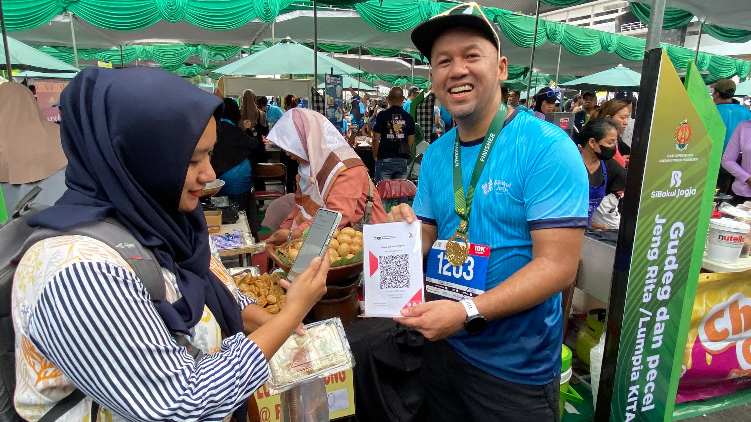 Direktur Finance & Strategy BSI Ade Cahyo Nugroho (kanan) saat melayani translaksi pembayaran QRIS pengunjung pada gelaran acara Sibakul Jogja Sport Fest 2024