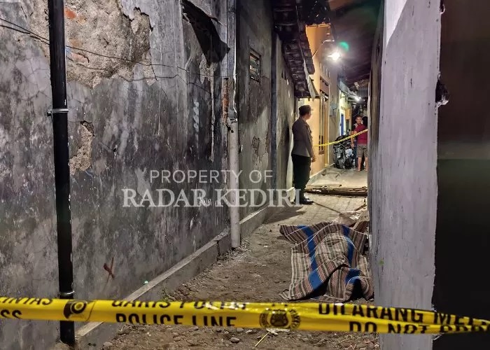 SEPTEMBER KELABU: Jasad Dadang ditutupi dengan tikar dan dijaga polisi di sebuah gang Kelurahan Balowerti, Kota Kediri. (FOTO: Novanda Nirwana/JPRK)