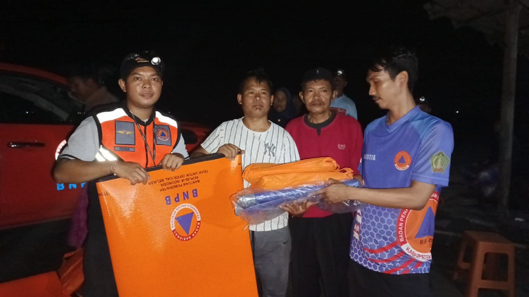 SERAHKAN BANTUAN : Petugas BPBD Jembrana menyerahkan bantuan terpal dan matras untuk warga terdampak puting beliung di Banjar Pebuahan, Minggu (8/12)