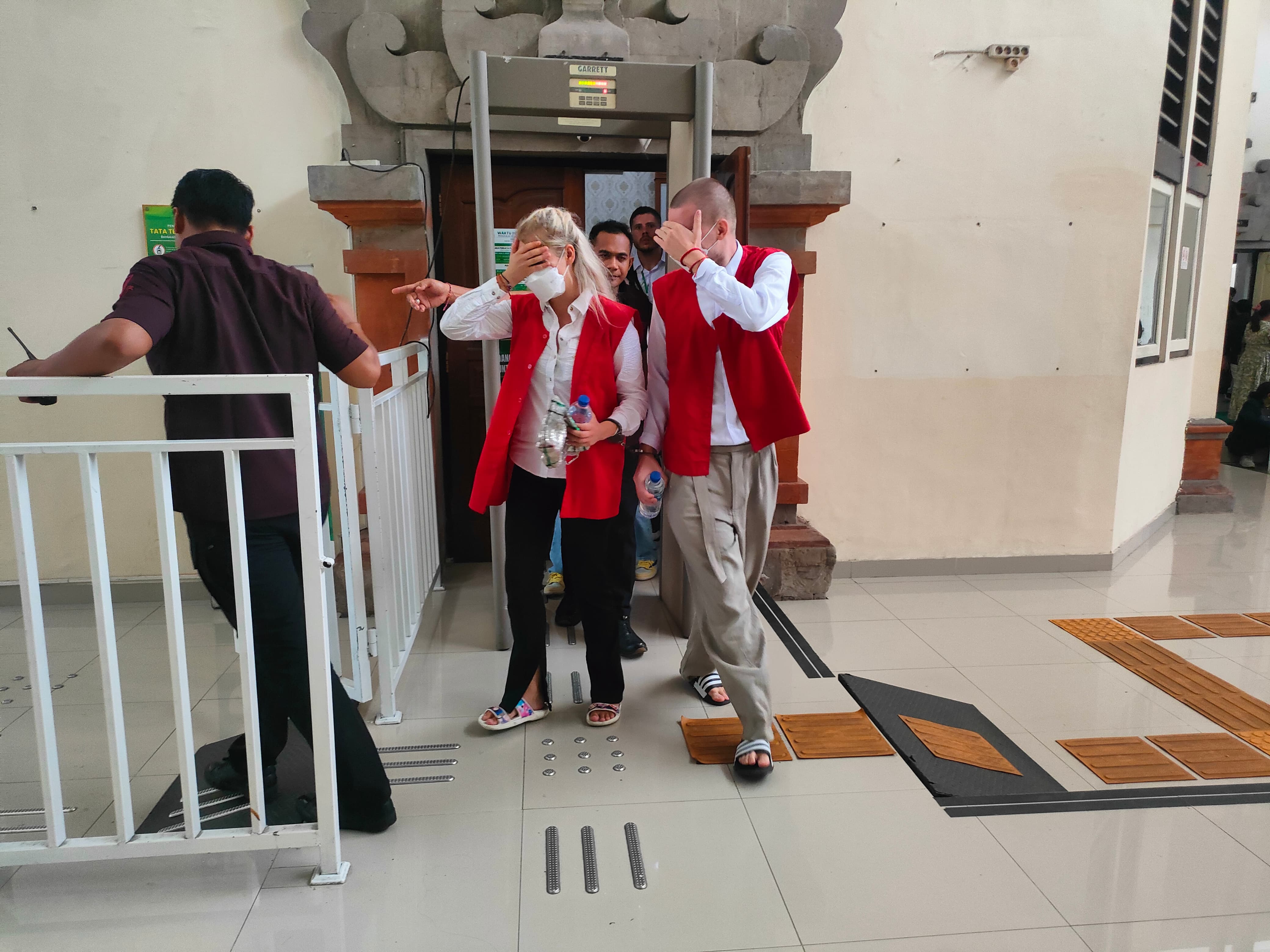 TUTUPI: Anastasiia Koveziuk dan Maxsim Tokarev menutupi wajah saat keluar dari ruang sidang. (Bali Express/I Gede Paramasutha)