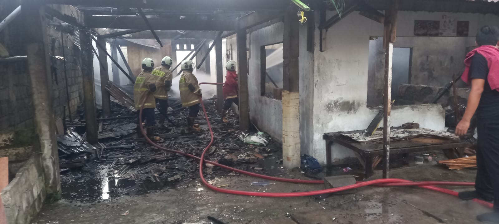 LUDES: Petugas Pemadam Kebakaran Kabupaten Badung melakukan pendinginan di bangunan kos semi permanen yang ludes diamuk si jago merah. (Bali Express/Istimewa)