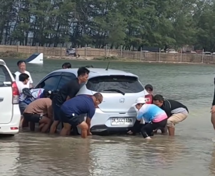 Warga bantu evakuasi pemilik mobil yang terendam  air laut di pantai Sanur