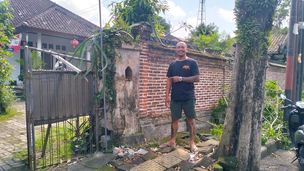 Made Surya Wirawan,42, warga di Jalan Kaswari, Banjar Jambe Baleran, Desa Dajan Peken, Kecamatan/Kabupaten Tabanan, menunjukan tembok pagar rumahnya ayang hampir roboh karena akar pohon perindang.
