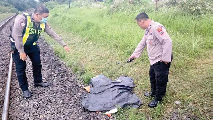 TANPA IDENTITAS: Dua personel Polsek Sukun mengevakuasi jenazah pria yang tewas setelah tertemper KA Penataran.