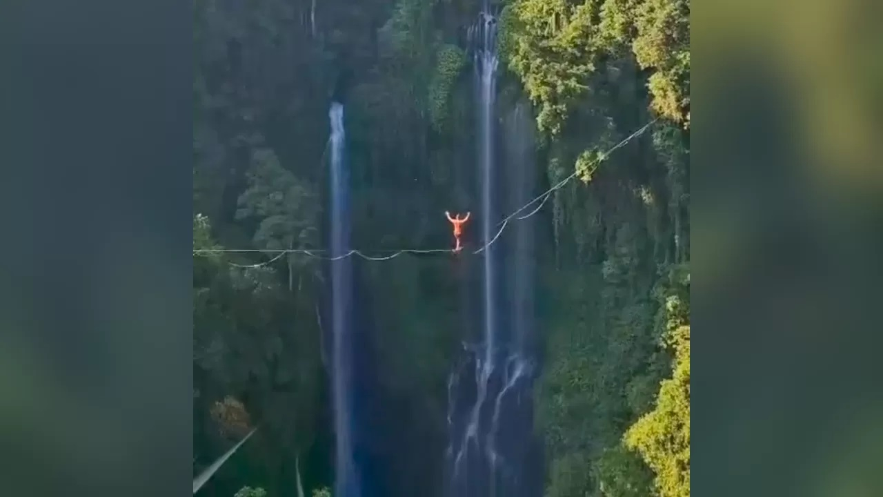 Seorang turis melakukan atraksi tight rope di atas tebing Air Terjun Sekumpul