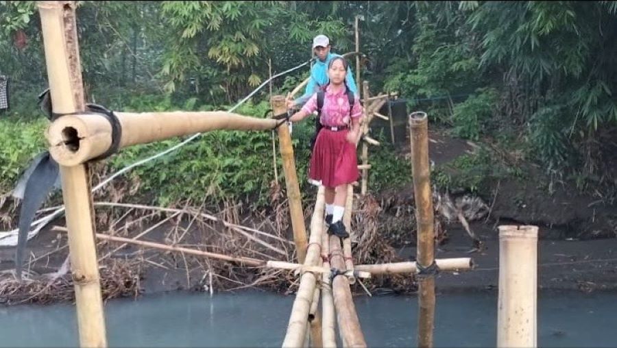 Warga menyeberangi jembatan bambu yang kondisinya miring dan rawan ambruk di Kelurahan Pendem, Jembrana.