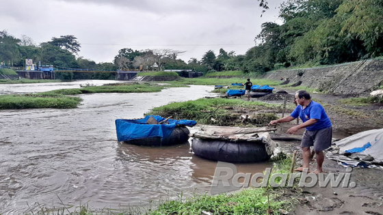 TAKUT HANYUT: Dimyati mengikat ban dengan kencang pada besi yang tertancap di bantaran sungai Dusun Jalen, Desa Setail, Kecamatan Genteng, Senin (11/7). JPG