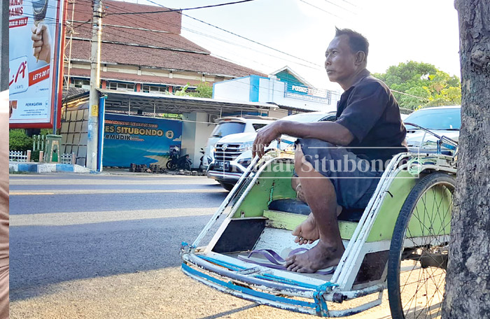 BERTEDUH: Samsiadi, 30, warga Desa Talkandang, Kecamatan/Kota Situbondo, menunggu penumpang di pinggir Jalan Raya utara Alun-alun Kota Situbondo, Selasa (21/11).