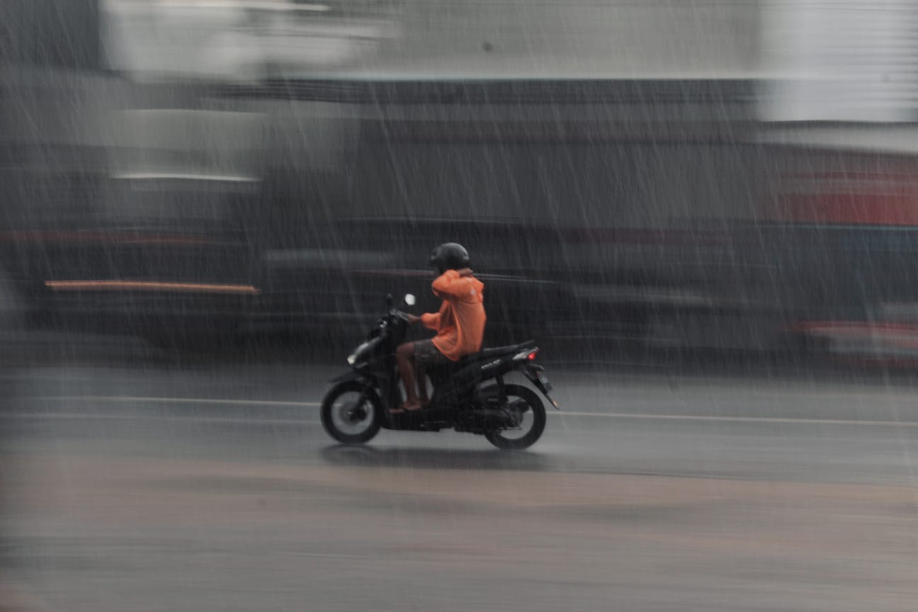 Ilustrasi pengendara motor diguyur hujan di jalan