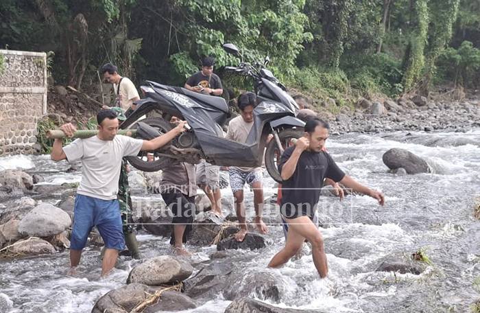 GOTONG ROYONG: Sejumlah warga menggotong sepeda motor akibat jembatan putus diterjang banjir, Minggu (25/1).